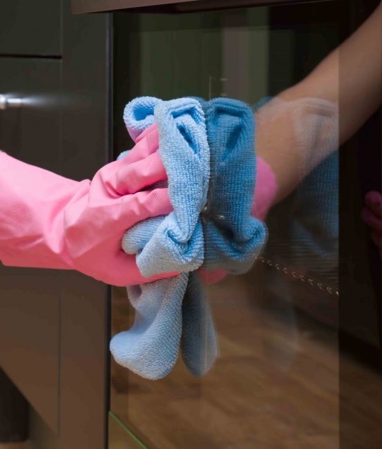 Employee hand in rubber protective glove with micro fiber cloth wiping an electric oven surface. Maid or housewife cares about house. Regular clean up. Commercial cleaning company concept.